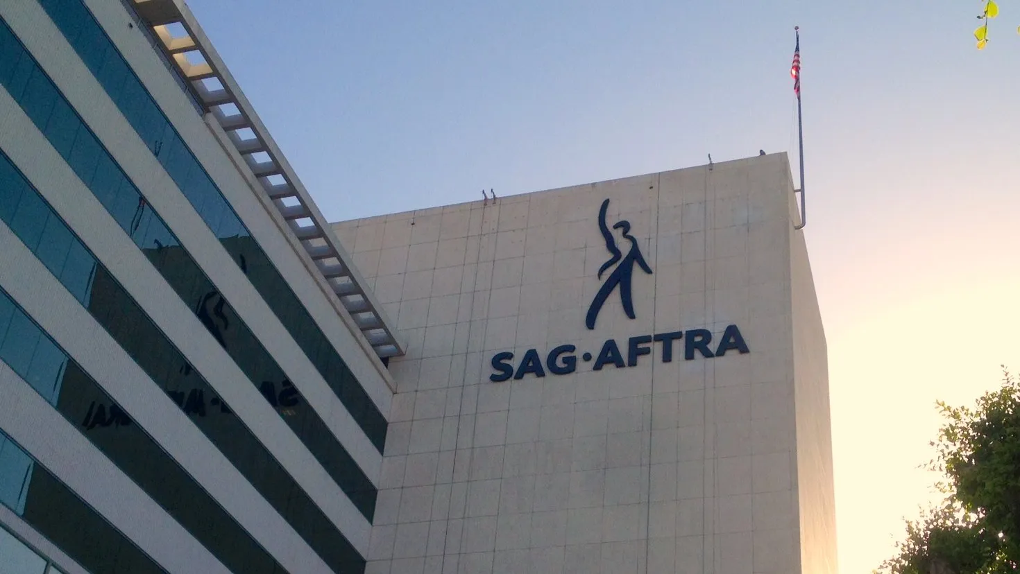 A SAG-AFTRA sign on the exterior of a building in daylight, photographed straight-on with a city street in the background