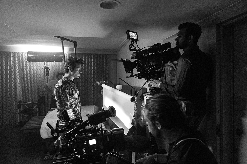 A behind-the-scenes photographer capturing a still image on a short film set, with a camera held up near a lit interior scene
