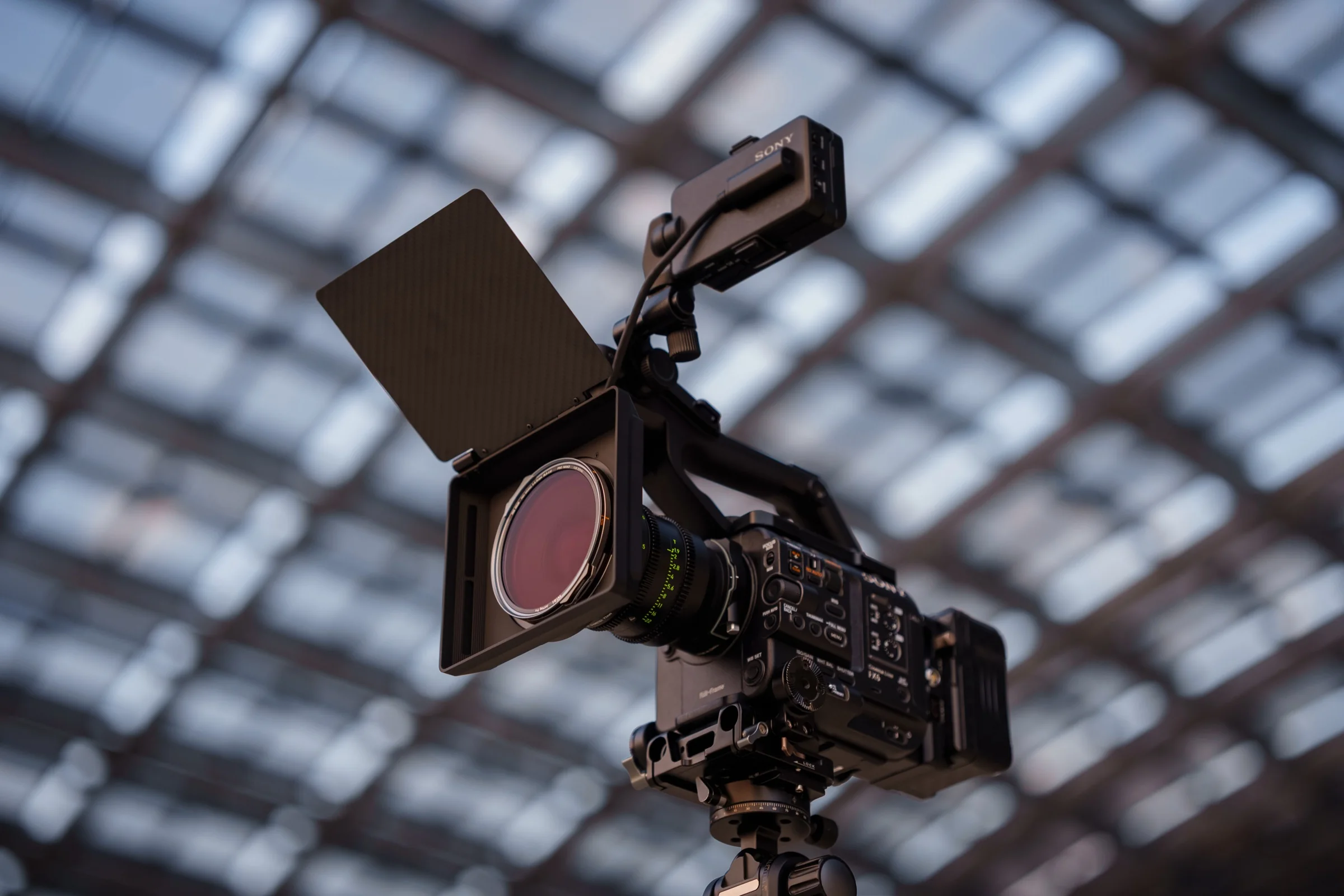 A behind-the-scenes view of a cinema camera with a large lens and matte box as crew members adjust equipment on set