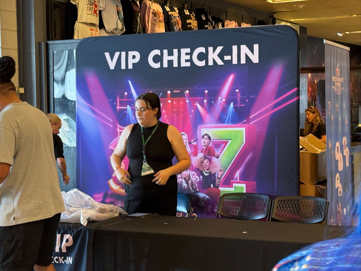 A concert venue lobby before doors open, with a VIP check-in table, stanchions, and staff assisting attendees