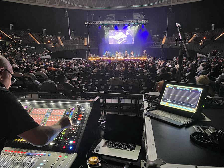 A concert venue sound booth positioned mid-room with mixing consoles and a clear view of the stage