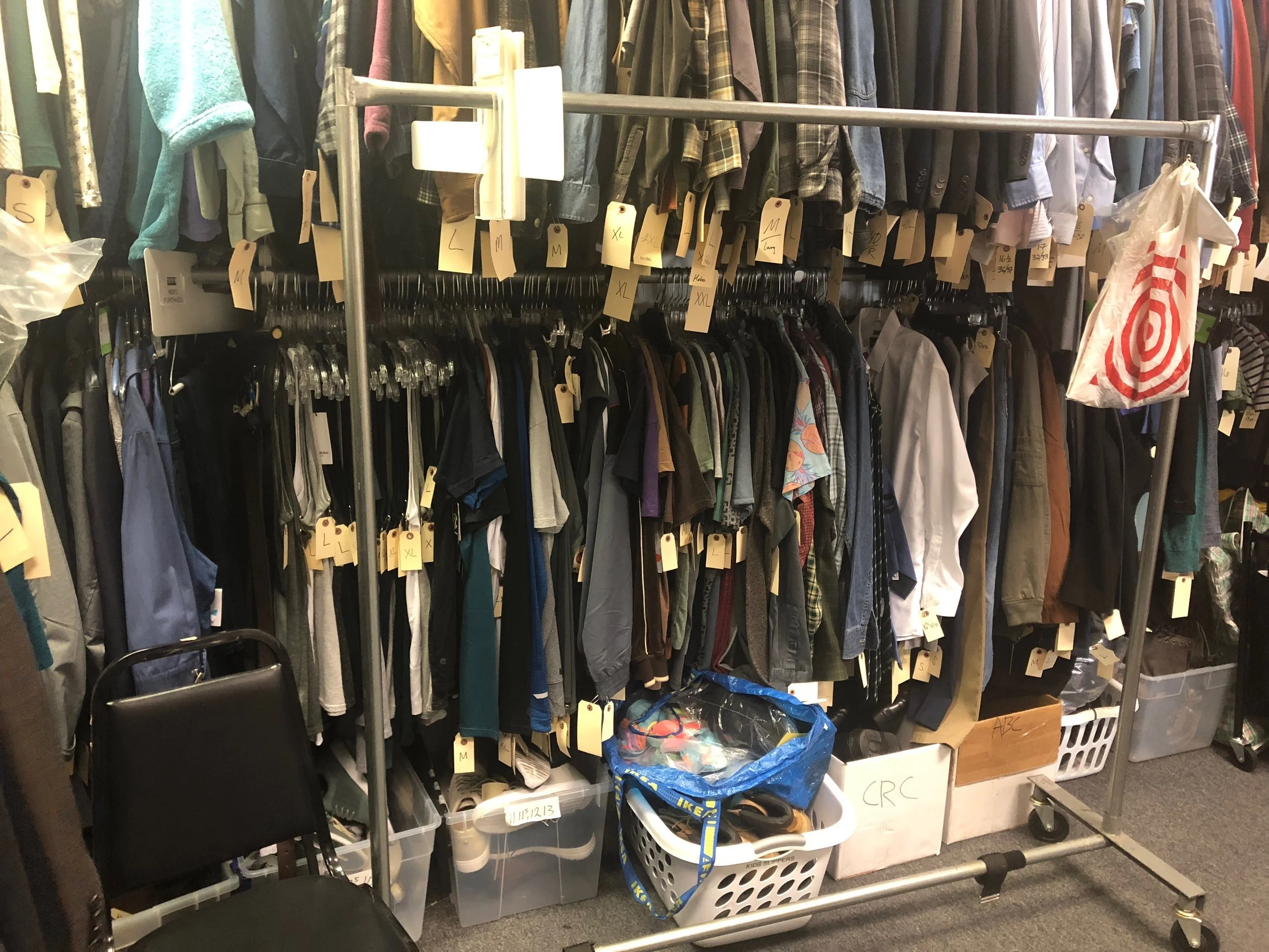 A costume rack on a working film set holding neutral jackets and shirts on hangers beside a rolling steamer