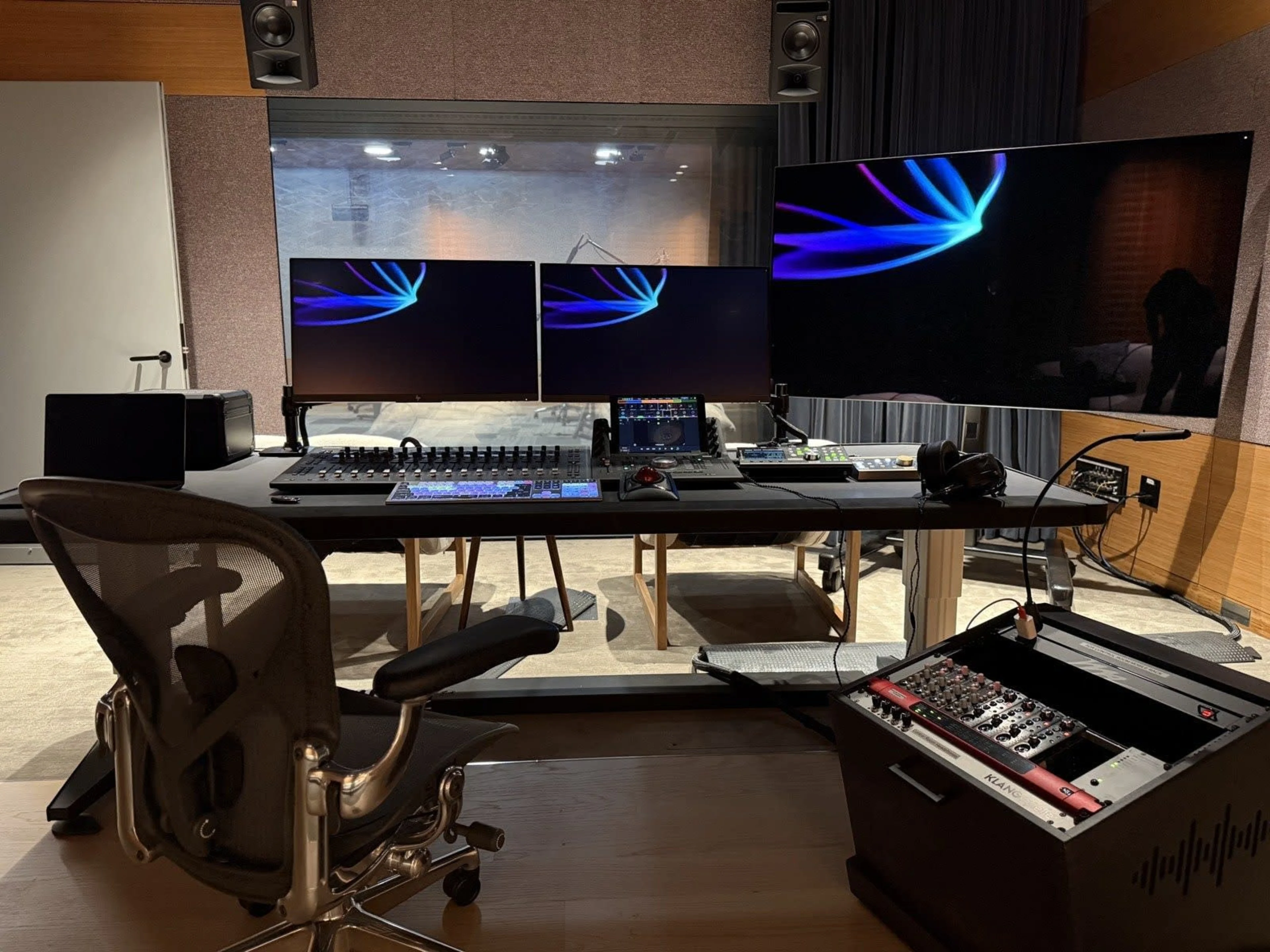 A dialogue editor in a dim post-production suite looking at a computer monitor with audio waveforms while studio speakers sit on either side of the screen