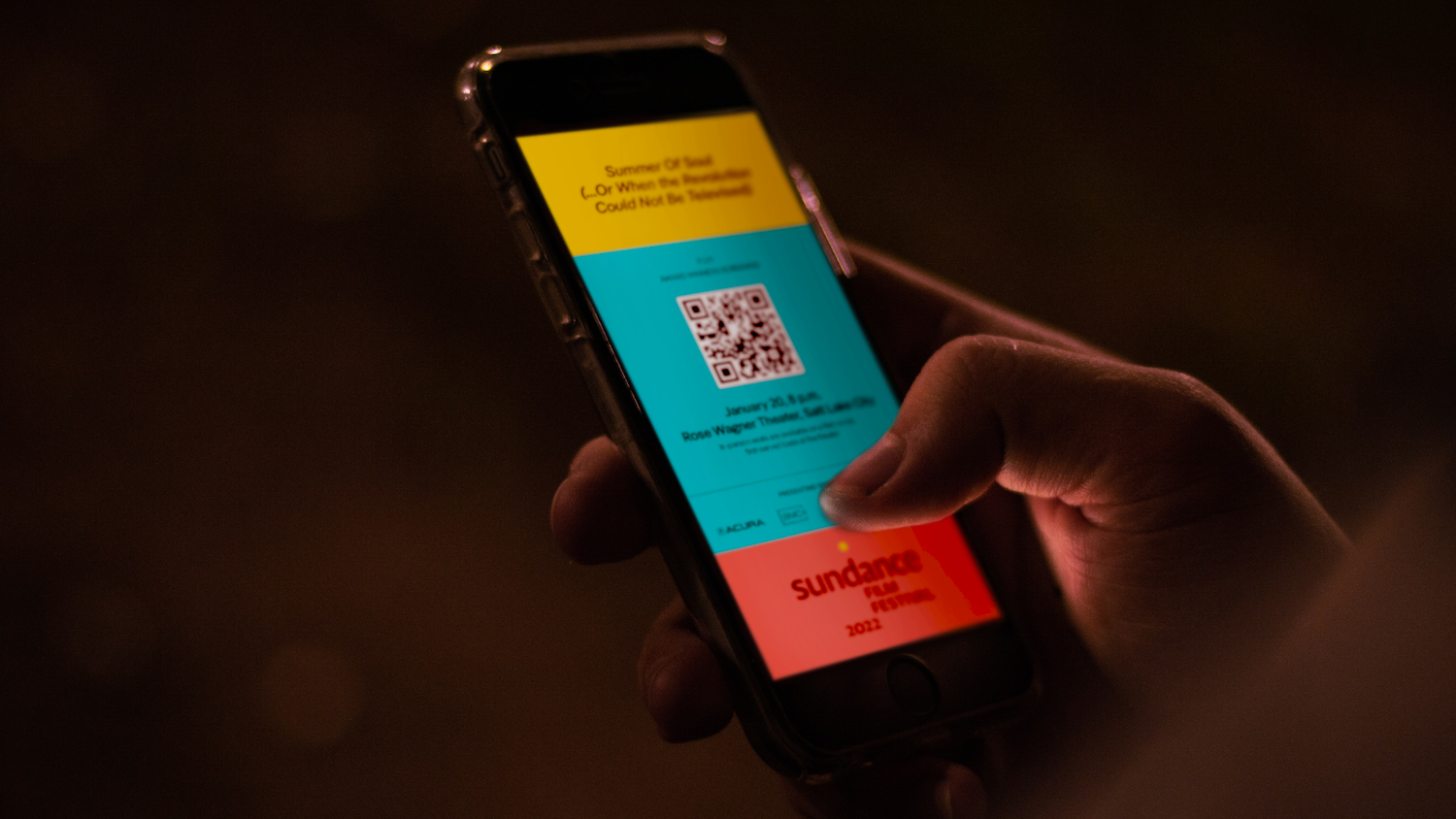 A festival staff member scanning a QR code on an attendee's phone at a theater entrance while the attendee holds a lanyard badge