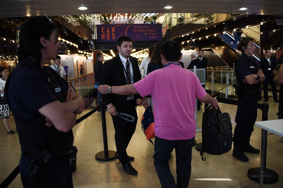 A film premiere security checkpoint outside a theater entrance, with staff checking guest credentials and small barriers guiding people into separate lines