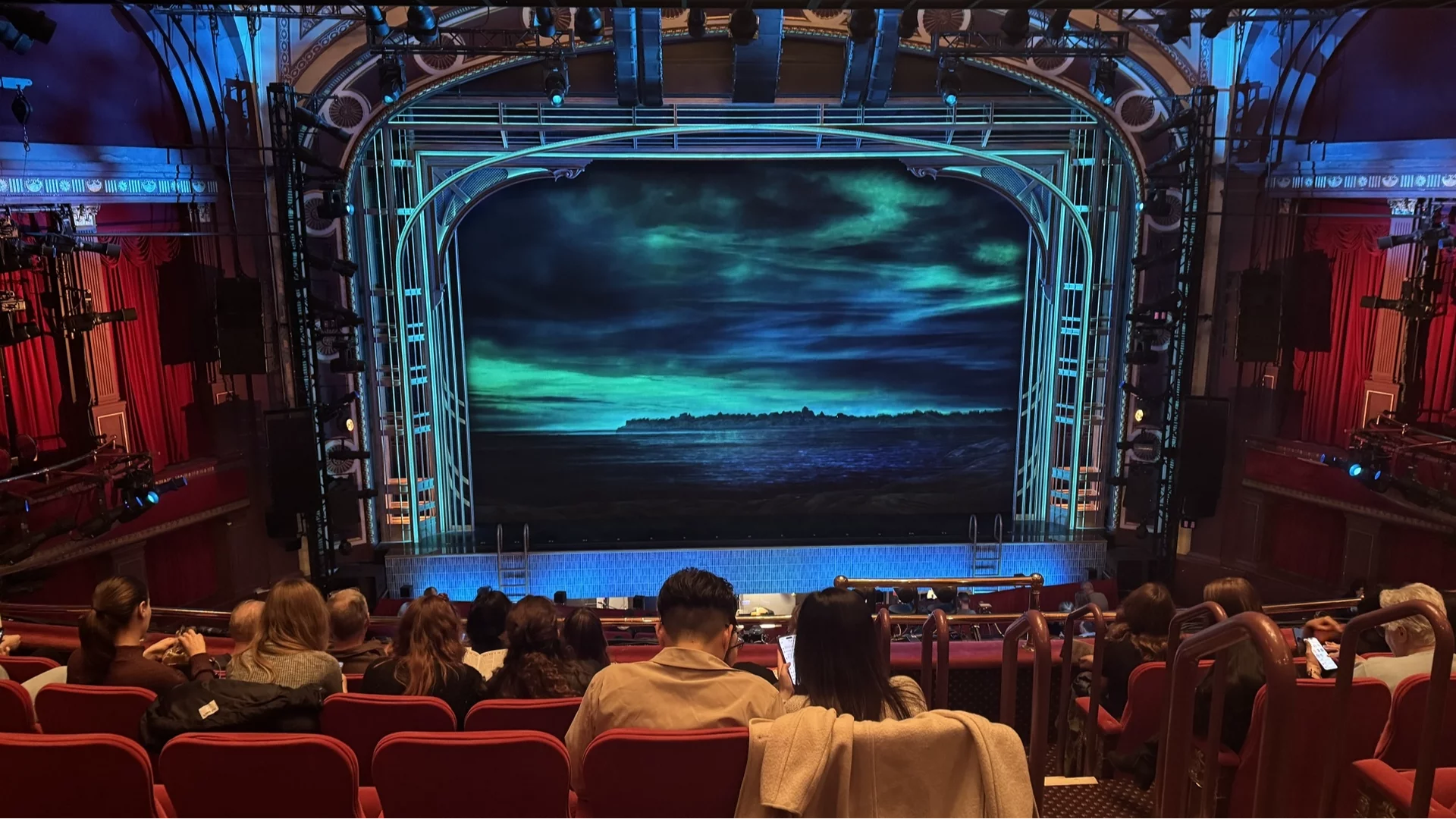 A full Broadway theater interior photographed from the mezzanine, showing the orchestra section, center aisle, and stage curtain before the show begins