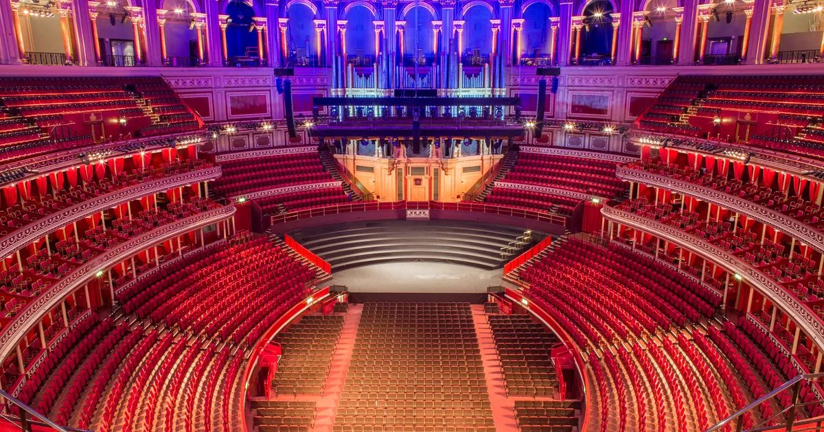 A high, wide view from a balcony seat in a grand circular concert hall, with the stage far below and rows of audience seating visible