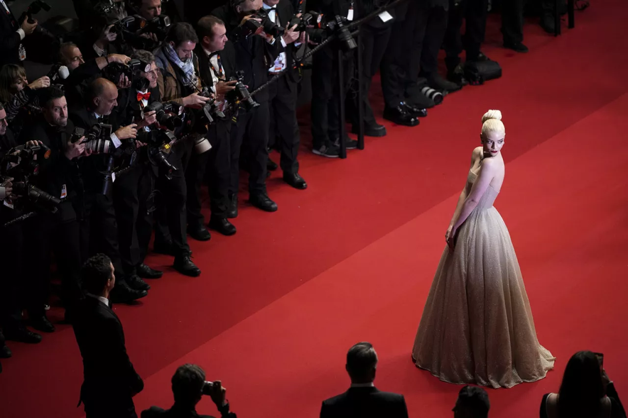 A line of guests in formal eveningwear stepping onto a red carpet outside a theater entrance at night, with photographers behind barricades and bright flash lighting