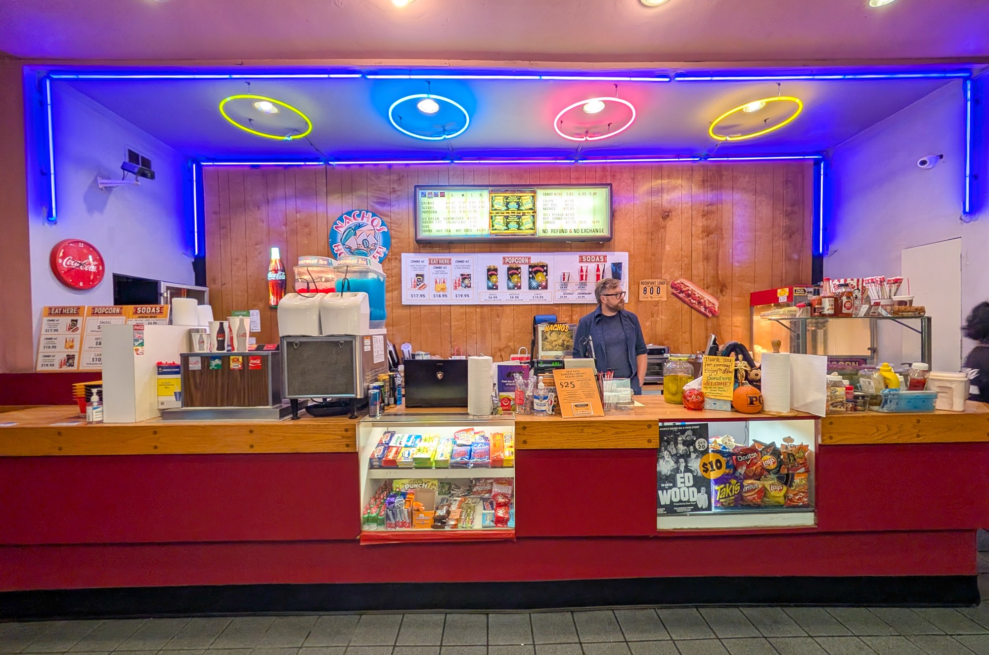 A movie theater concession stand with popcorn machines glowing and a staff member serving customers under warm lights