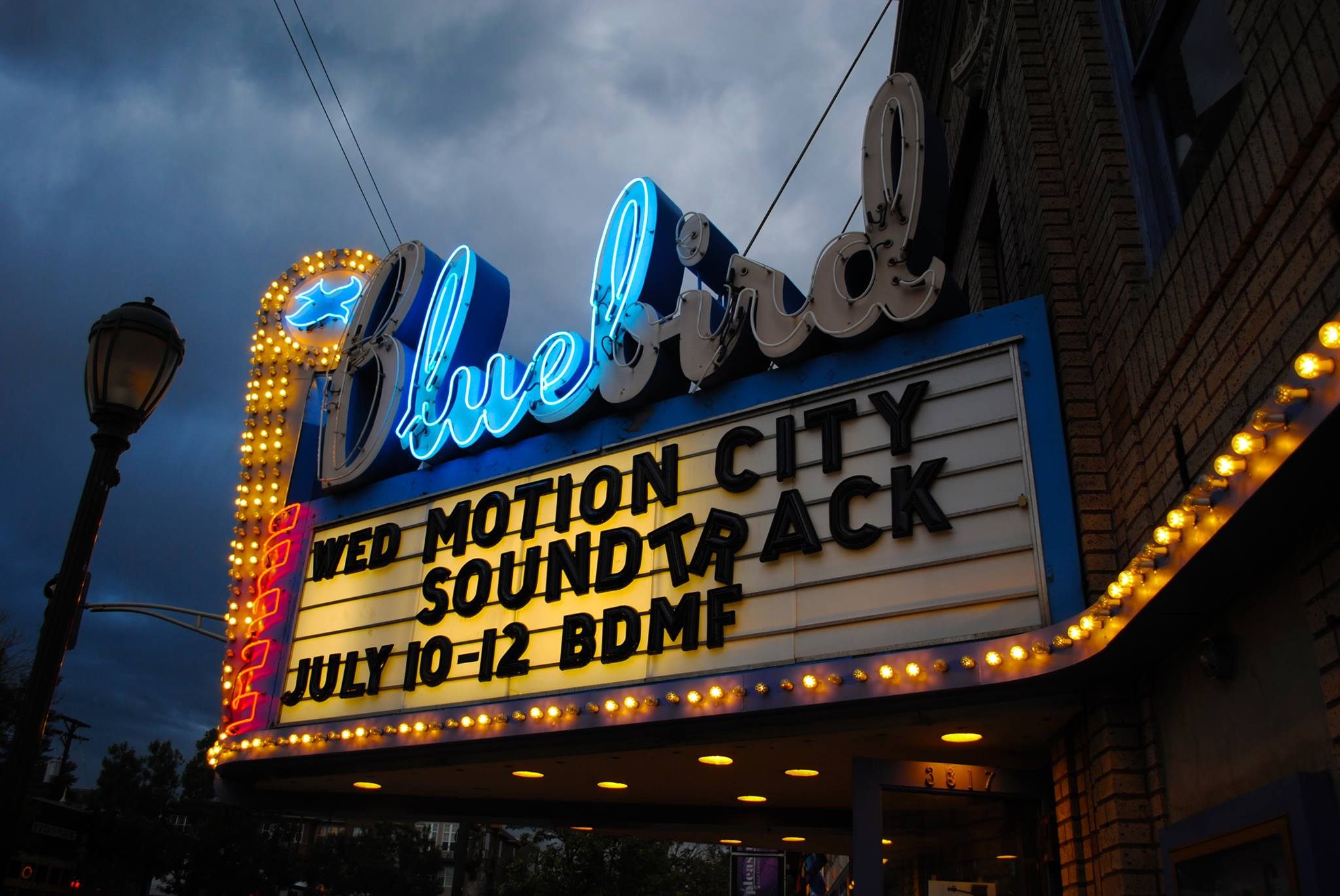 A nighttime view of a classic movie theater entrance with a glowing marquee and patrons lining up under warm lights