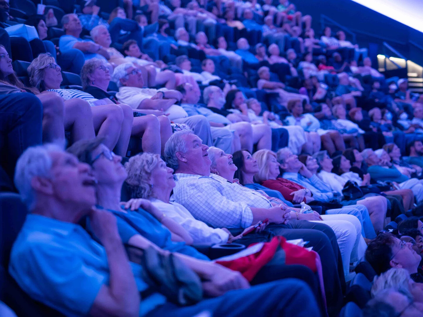A packed modern movie theater auditorium with a huge screen and rows of viewers settling into their seats before a screening
