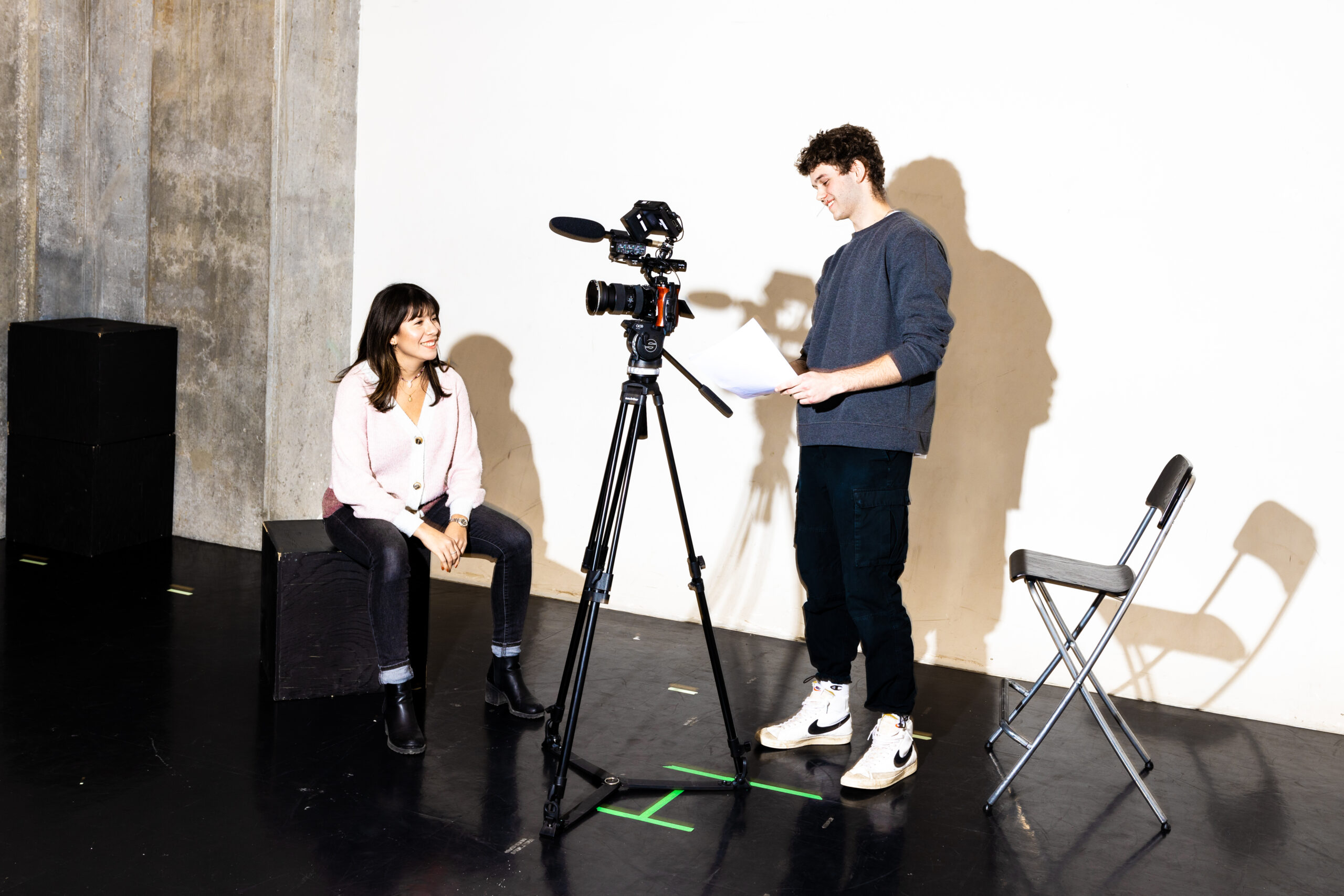 A performer in a quiet apartment filming a self-tape audition on a smartphone mounted to a tripod, with a neutral backdrop behind them