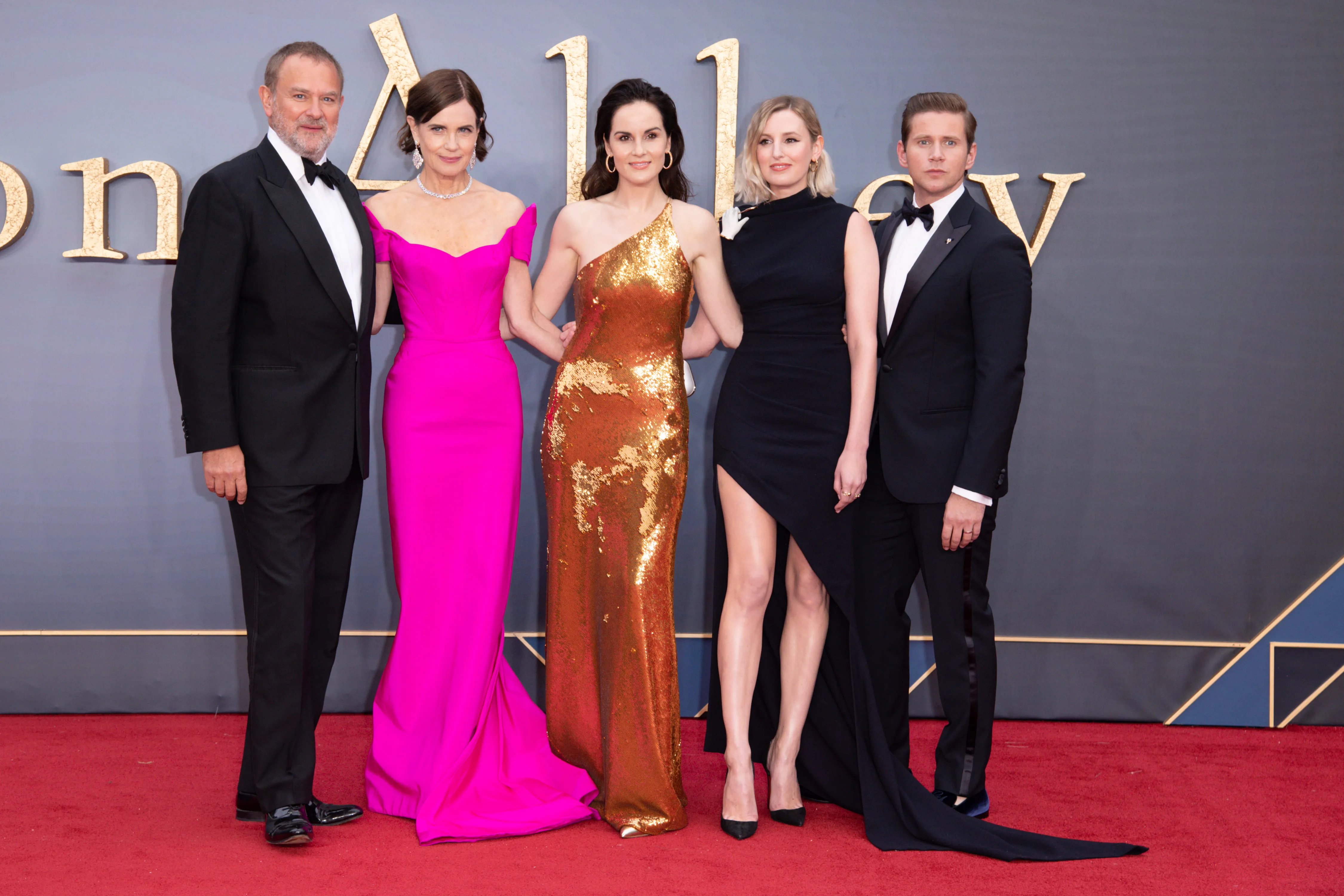 A red carpet outside a movie theater at night with photographers behind barricades and guests arriving in formal outfits