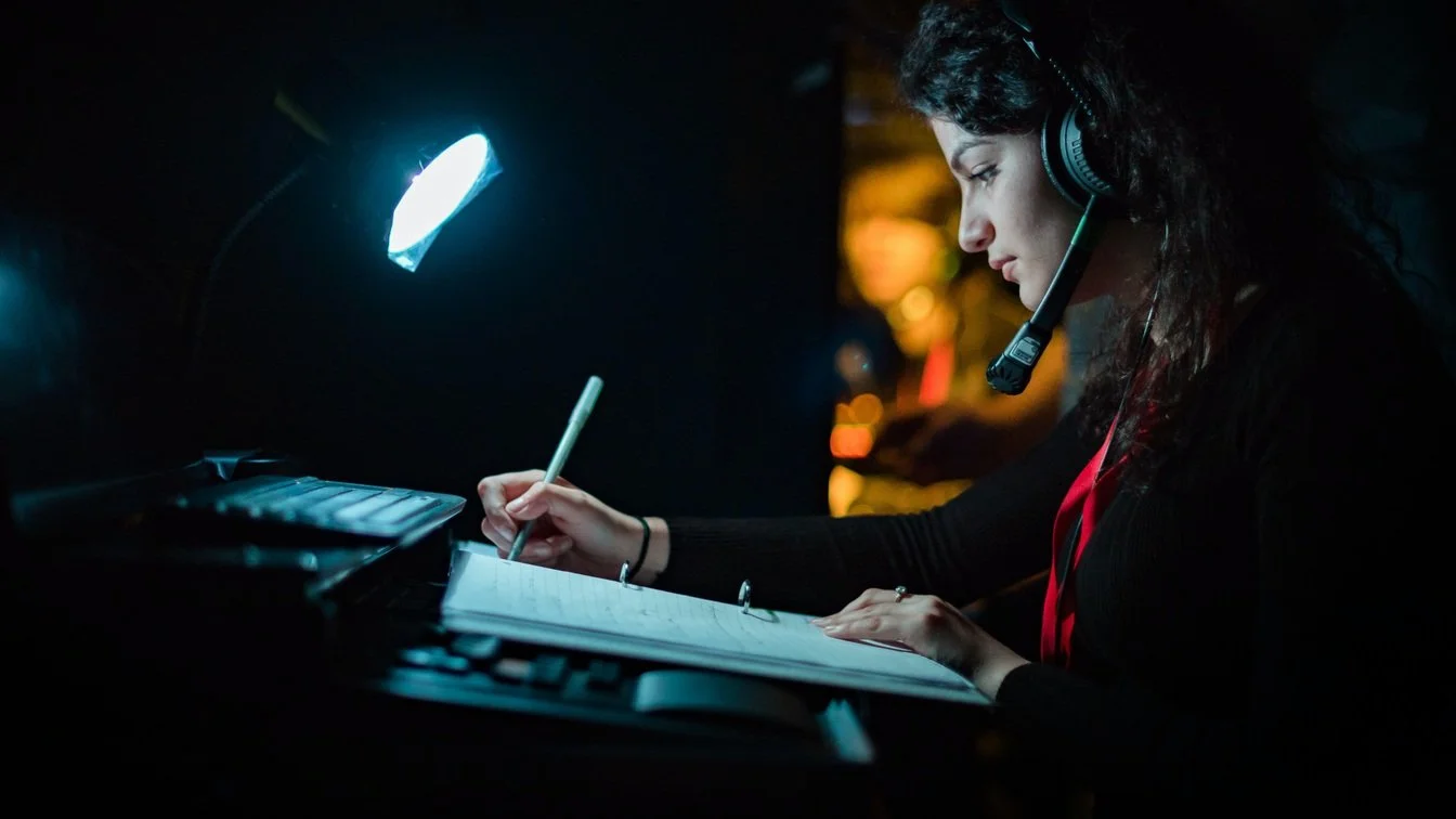 A stage manager at a calling desk wearing a headset, monitoring cue screens during a live performance