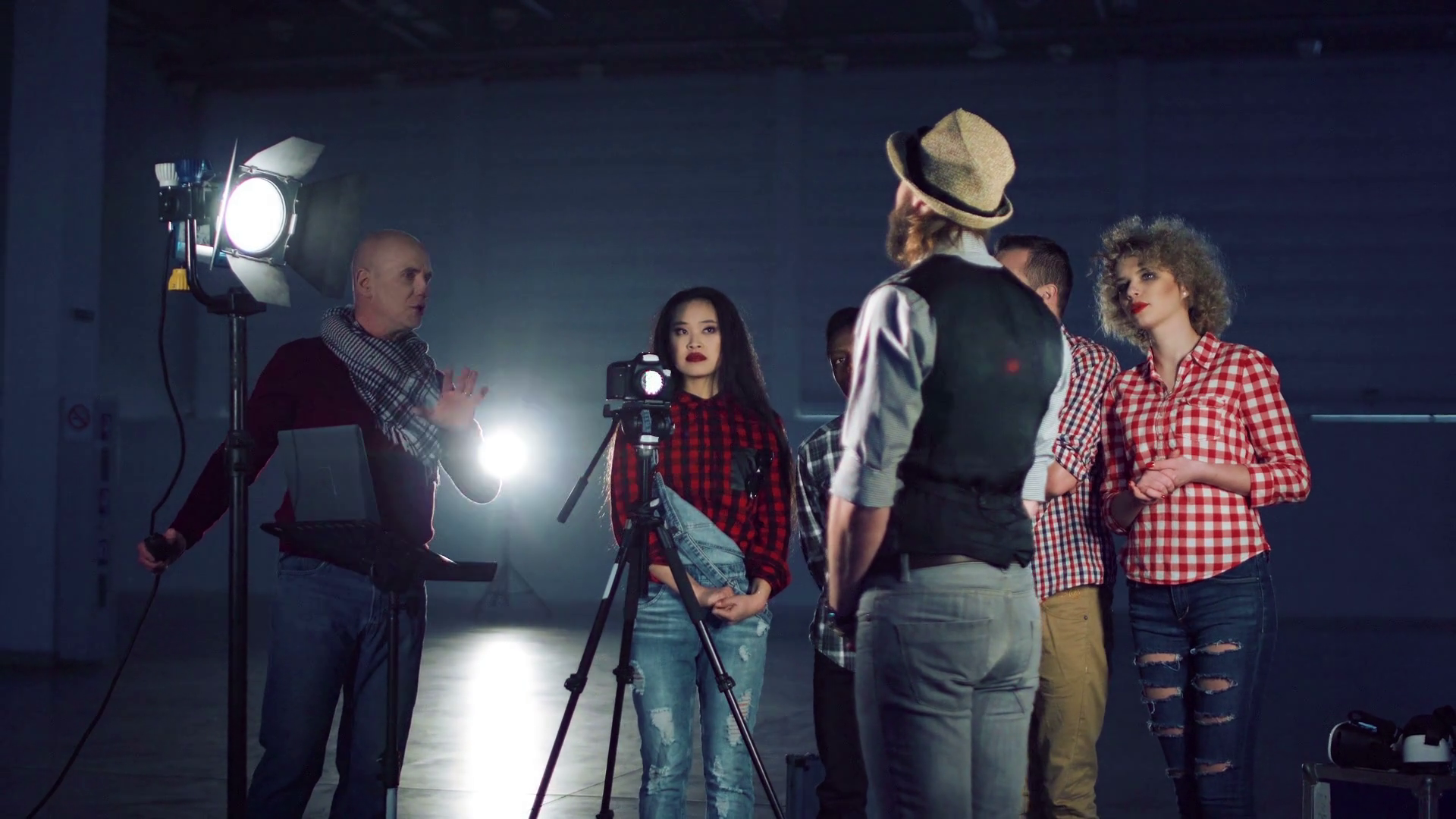 A stand-in actor standing on a taped floor mark while a cinematographer and gaffer adjust lighting and camera position on a professional film set