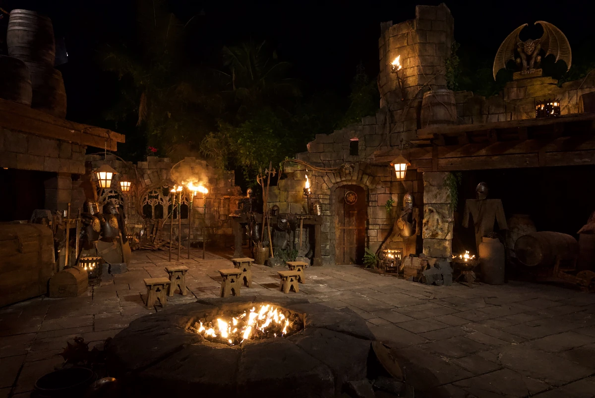 A torch-lit Survivor Tribal Council set at night with wooden benches arranged around a central fire