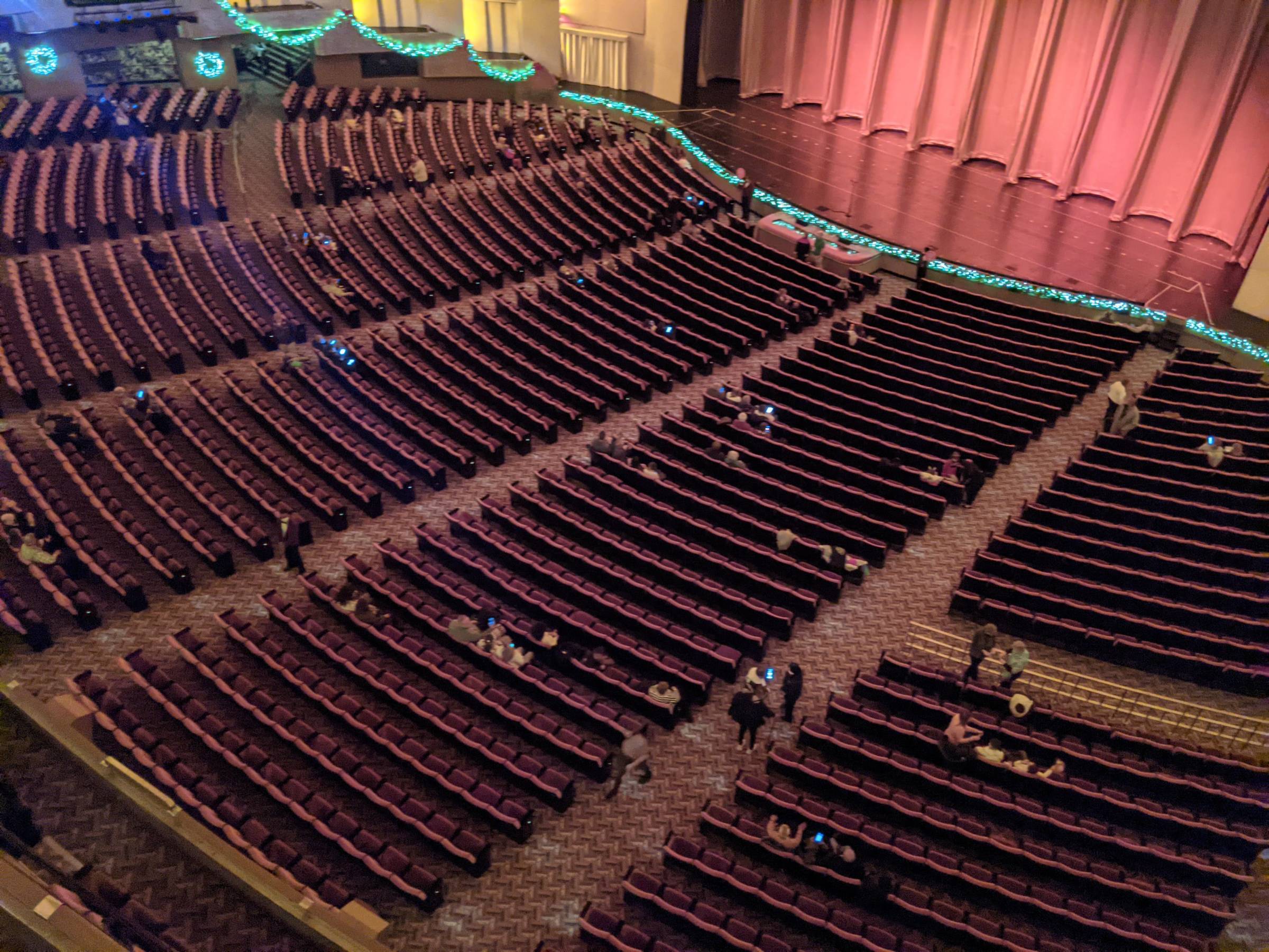 A view from the orchestra section of a large theater, showing rows of seats leading toward a brightly lit stage with curtains