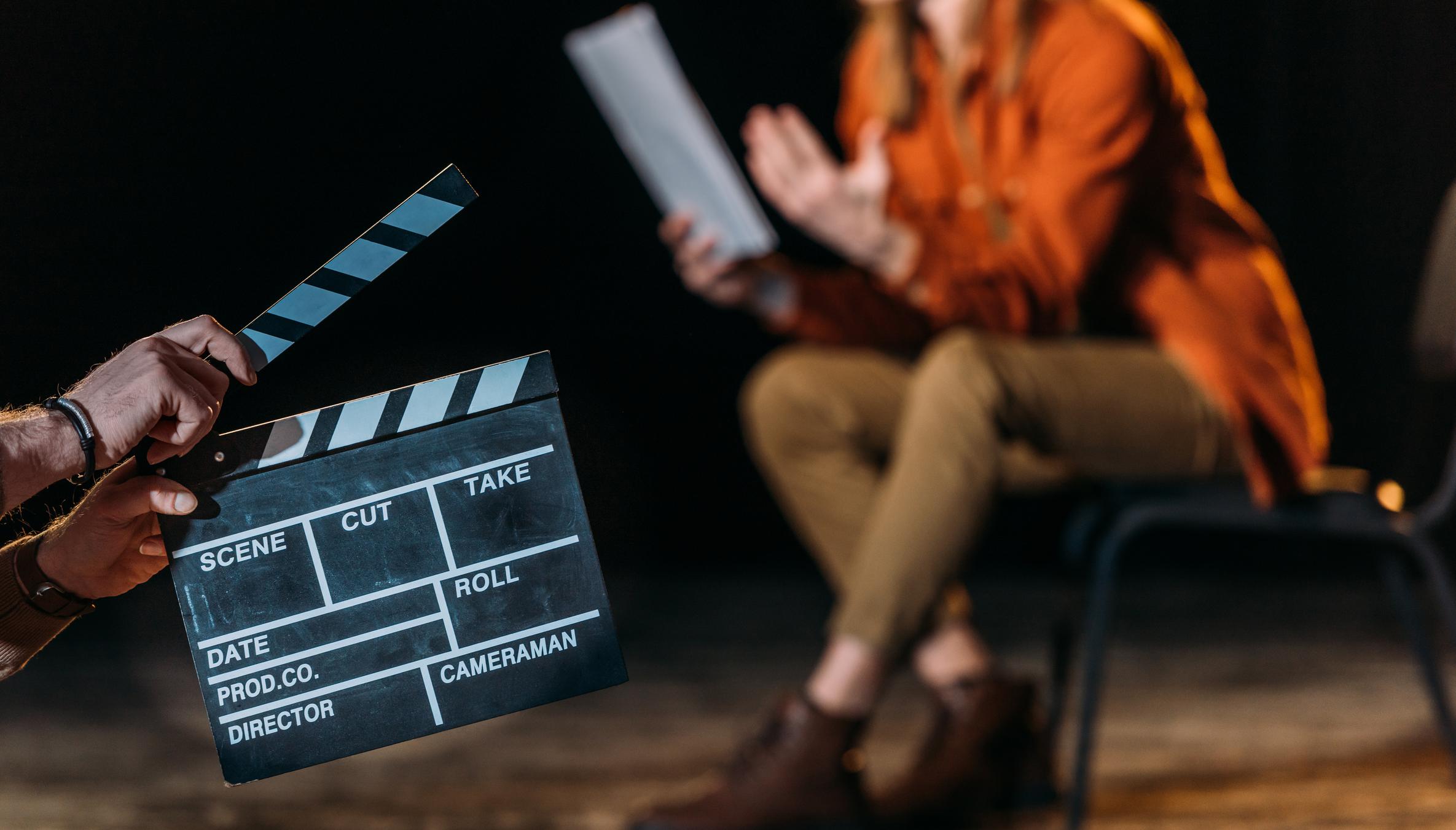 An actor standing in a casting studio against a plain backdrop, holding a resume and headshot, preparing to slate for a commercial audition
