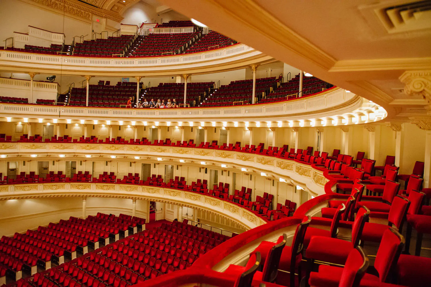 An angled view from a first-tier mezzanine level in an ornate concert hall, showing the stage below and curved rows of seats