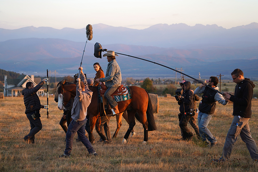 An assistant director holding a clipboard while speaking with background actors near a film set staging area