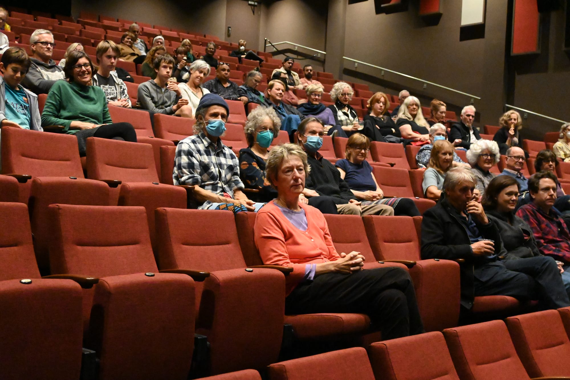 An audience seated in a small theater watching a film festival shorts block, with soft stage lighting and a screen glowing at the front