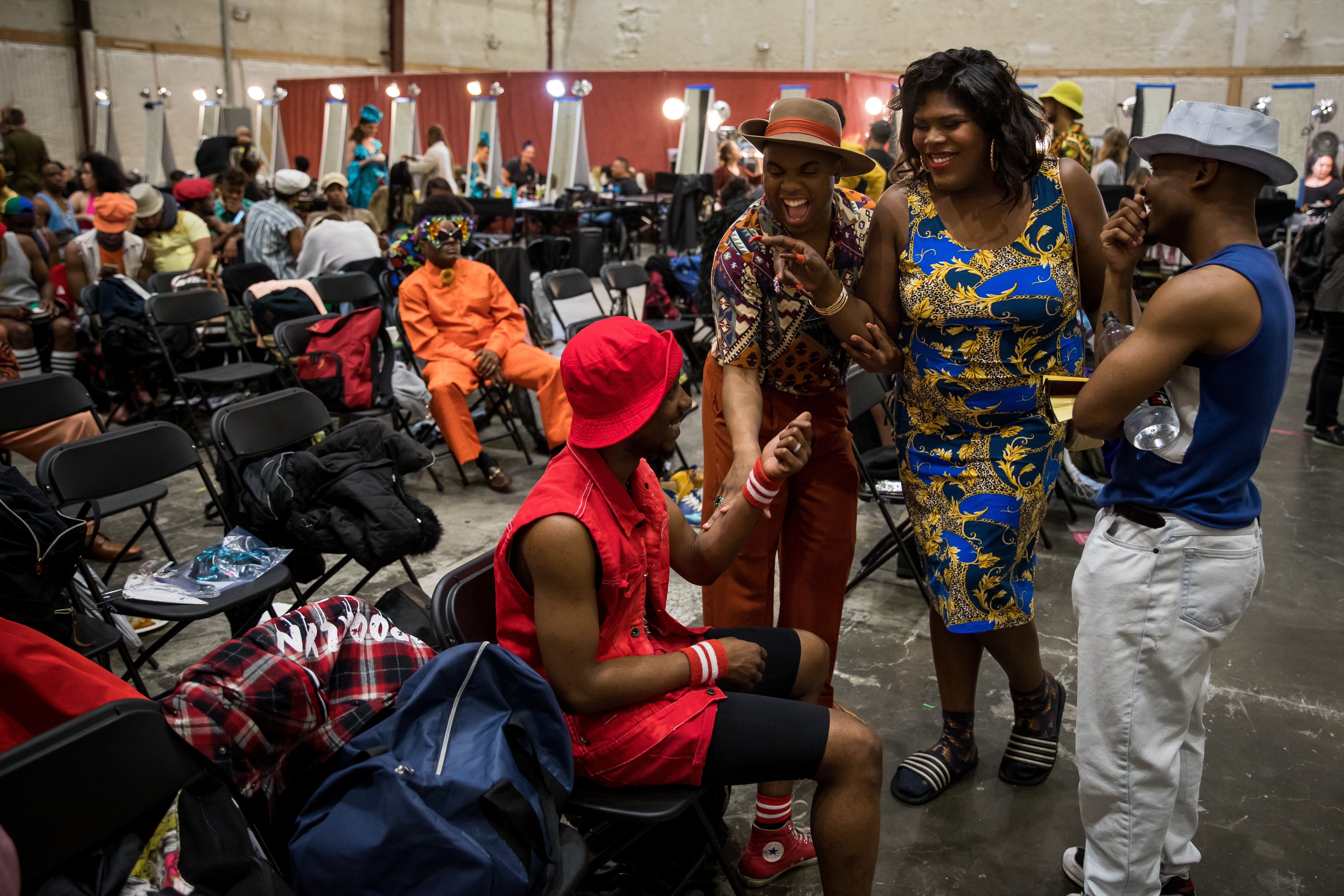 Background actors sitting in a quiet holding area on folding chairs with personal bags and water bottles, waiting for their call to set