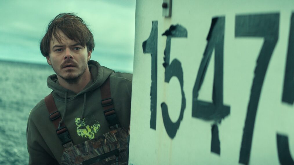 Charlie Heaton as Wade Penney, wearing practical workwear near a fishing village dock under overcast skies