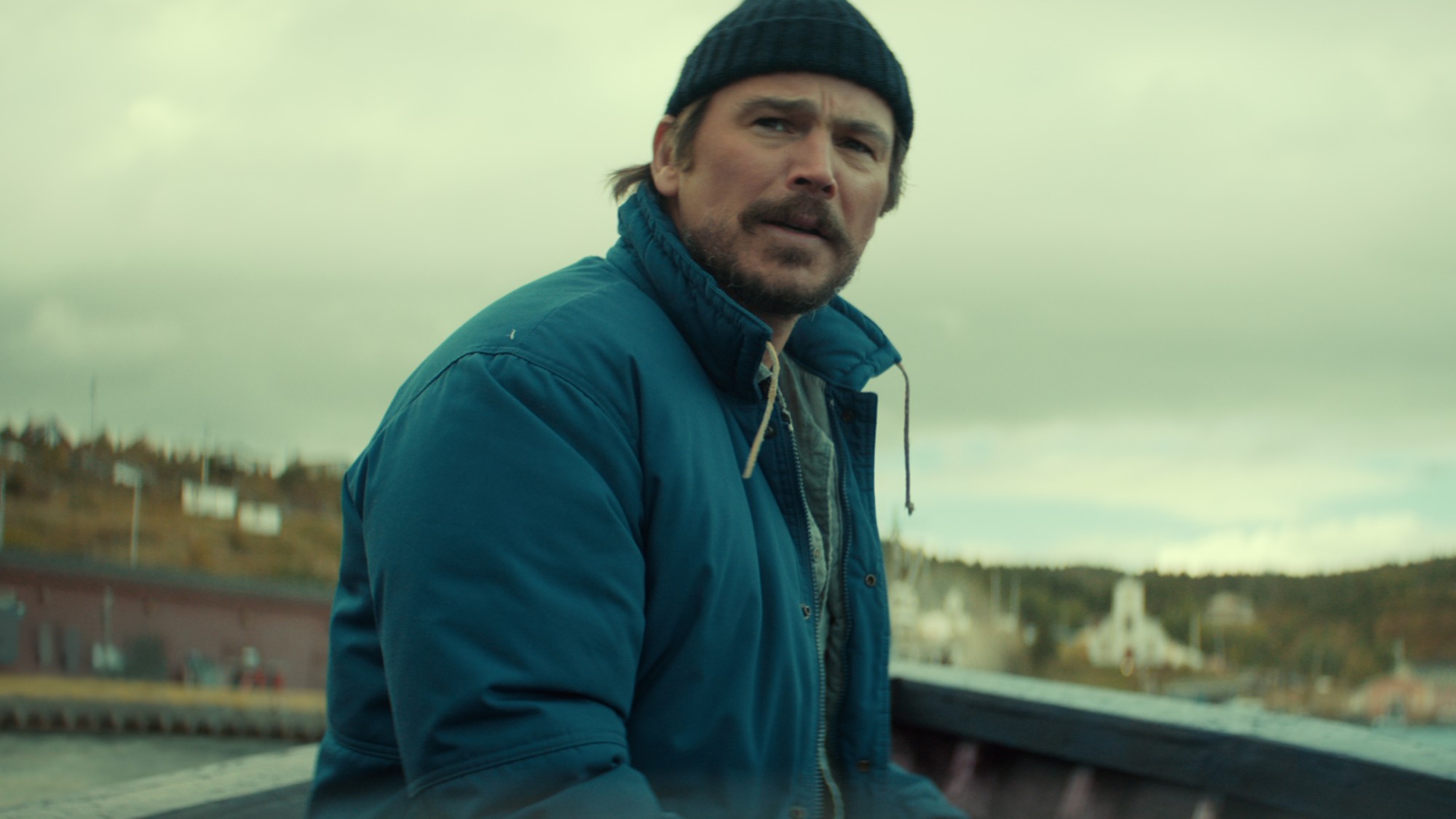 Josh Hartnett as Calvin Penney, outdoors in a foggy Newfoundland fishing village near the water, wearing rugged cold-weather layers
