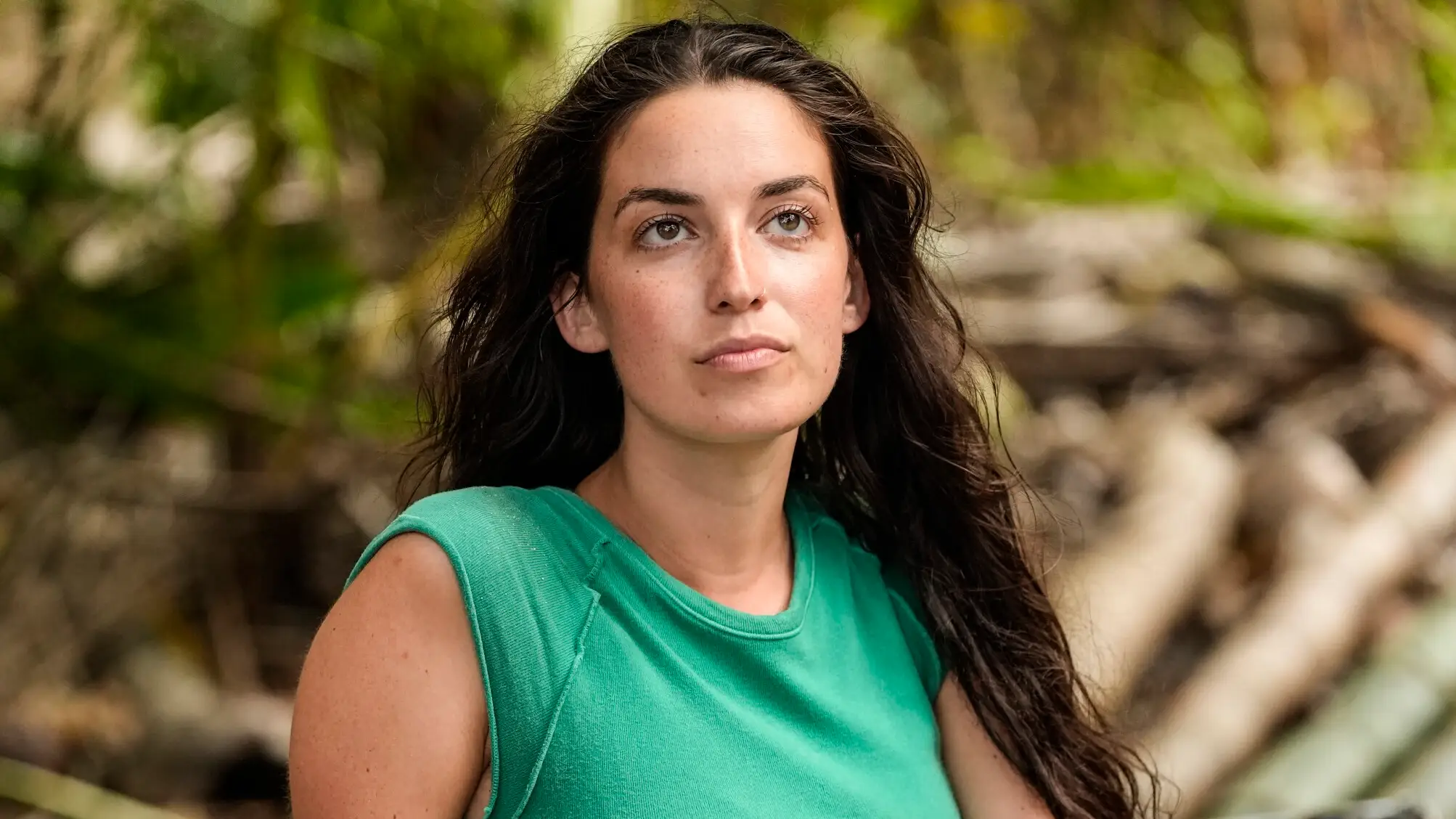 Linnea Capobianco at a torch-lit Tribal Council set at night, listening intently as other castaways look on