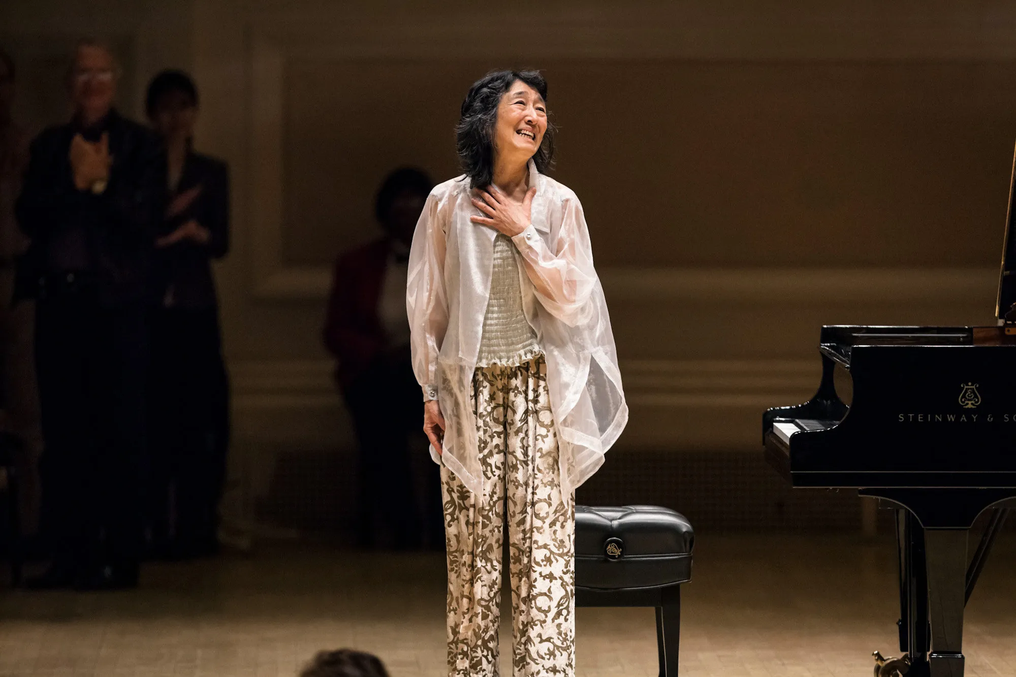 Pianist Mitsuko Uchida seated at a grand piano onstage inside Carnegie Hall, captured mid-performance under warm concert lighting