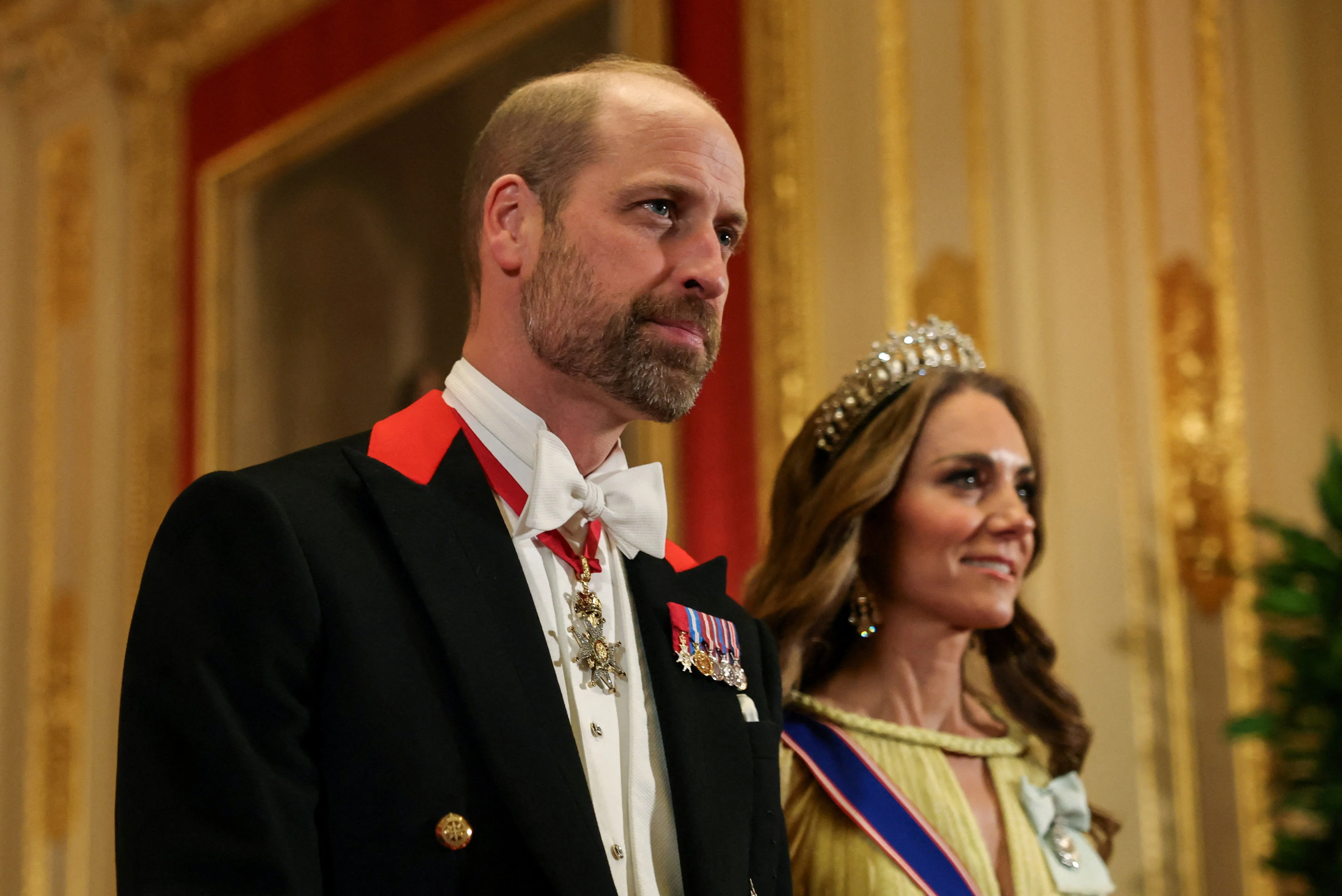 Prince William in formal evening wear at a state banquet, photographed in a grand palace room with warm lighting and ceremonial decor, news photography style