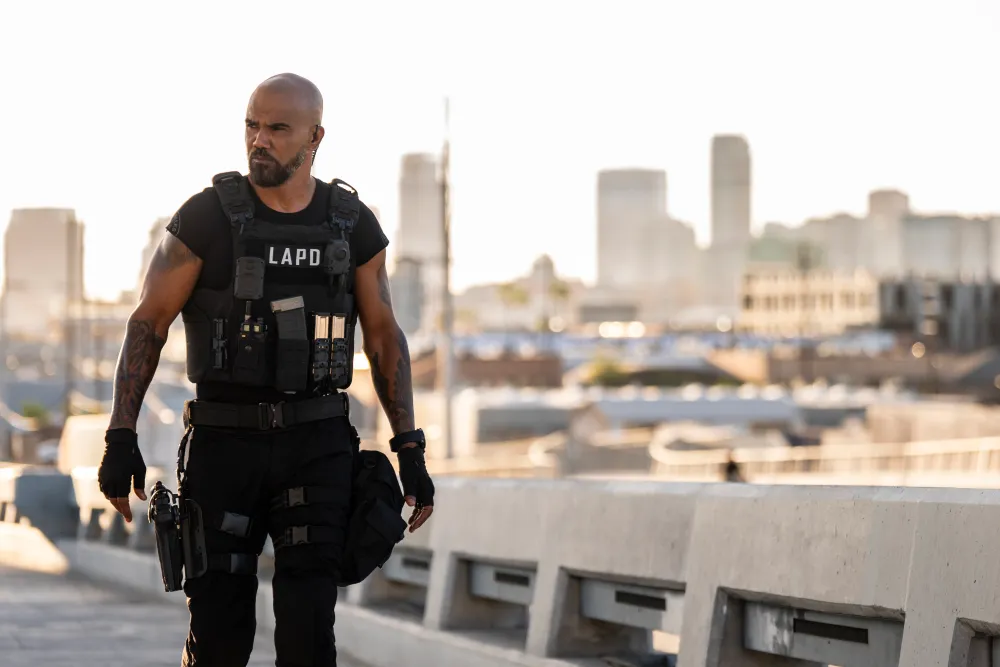 Shemar Moore on a set environment, dressed in dark tactical-style wardrobe, standing in a dramatic action-drama lighting setup, candid entertainment photography