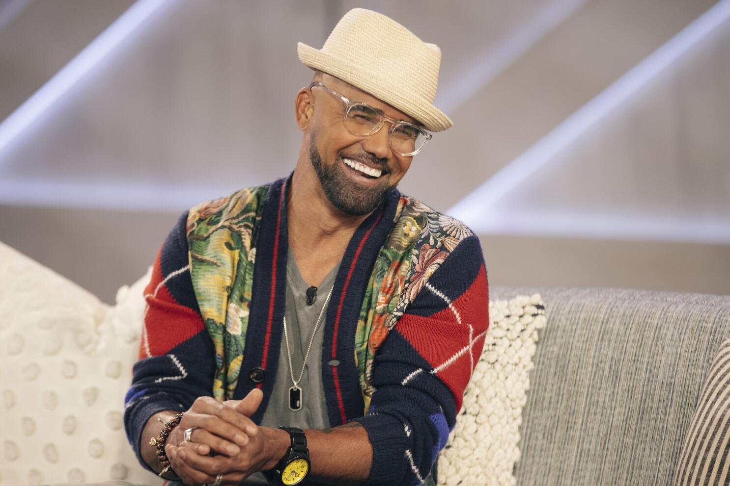 Shemar Moore seated in a studio interview setting under bright broadcast lights, wearing a tailored jacket, mid-conversation with an off-camera host