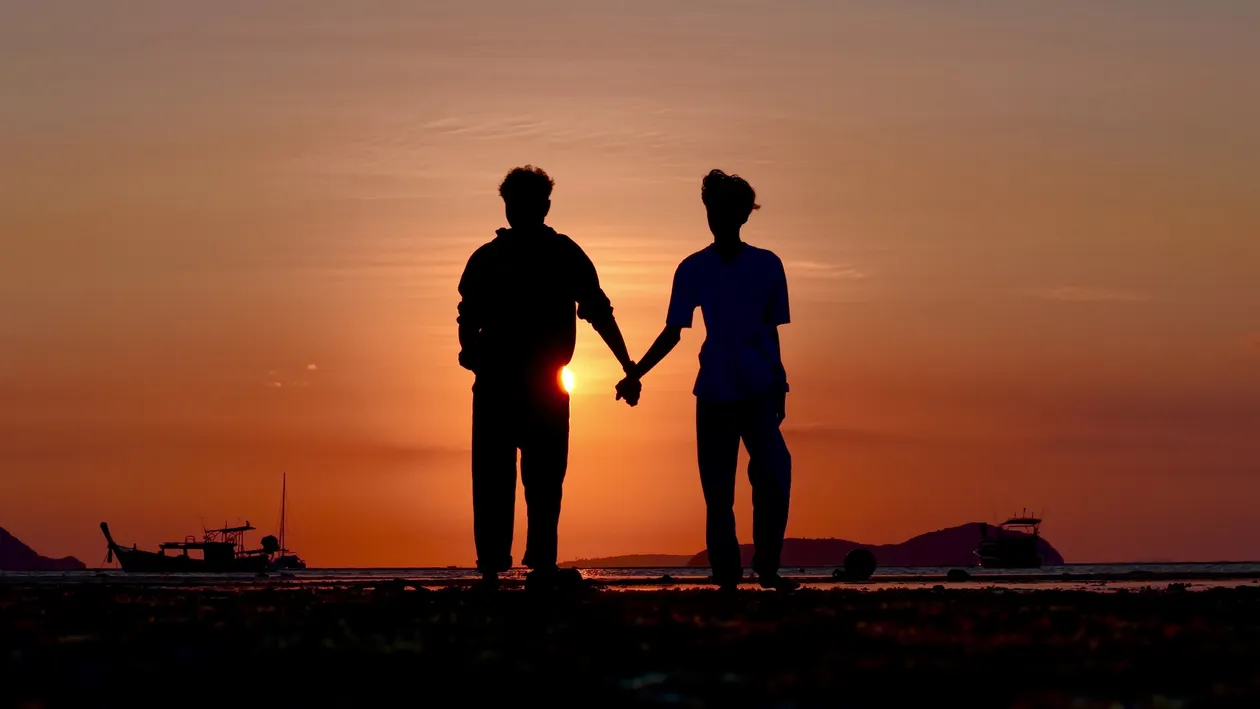 Silhouette of a couple standing on a beach at sunset, with warm light and calm water, capturing a reflective memory of the engagement moment.