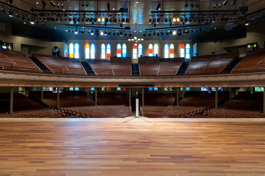 The Ryman Auditorium stage in Nashville viewed from the seating area, with warm wood tones and stage lighting set for a live performance