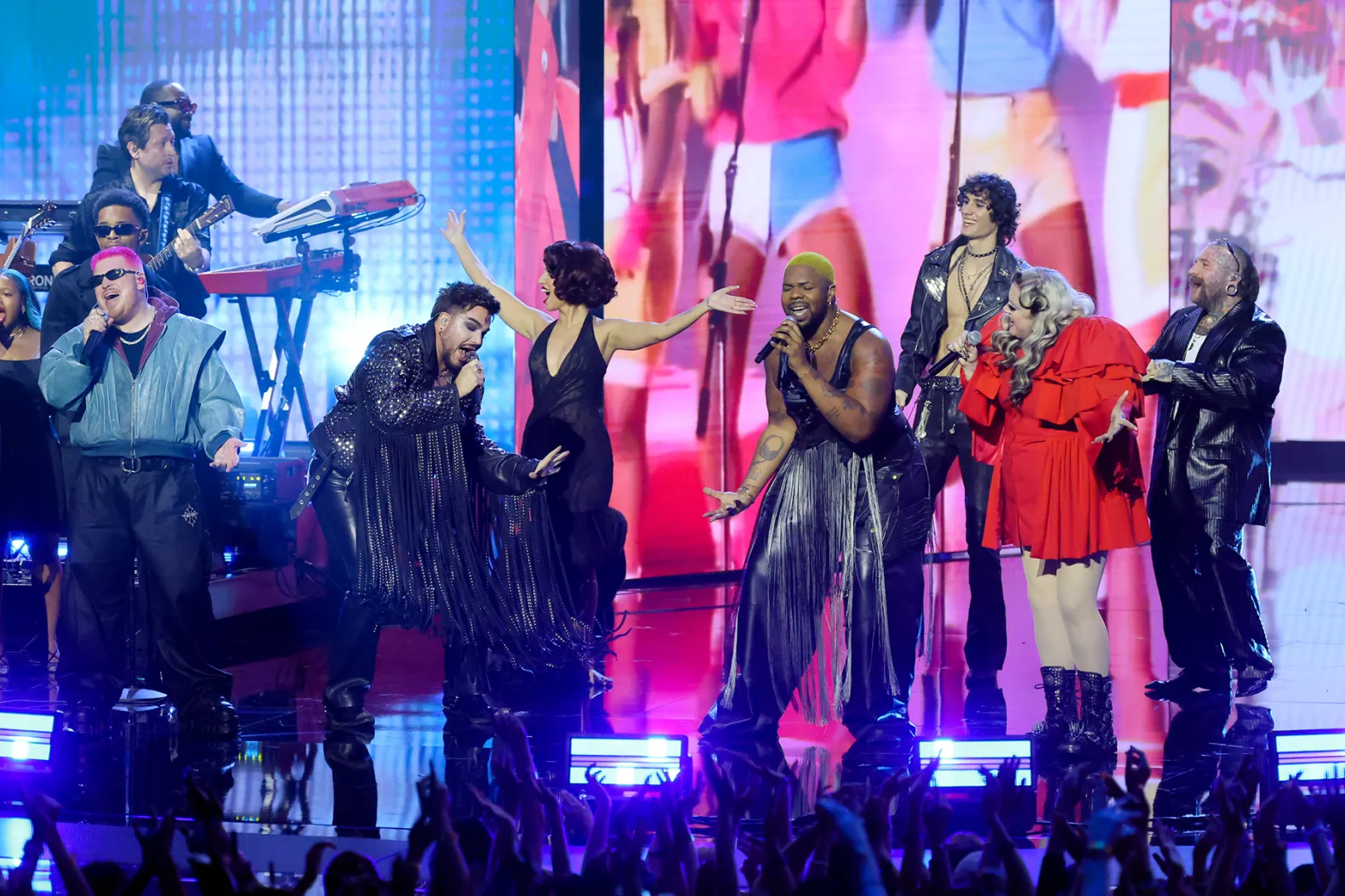 Two artists sharing a microphone on the VMAs stage mid-song, with a burst of backlight and the crowd visible beyond the footlights