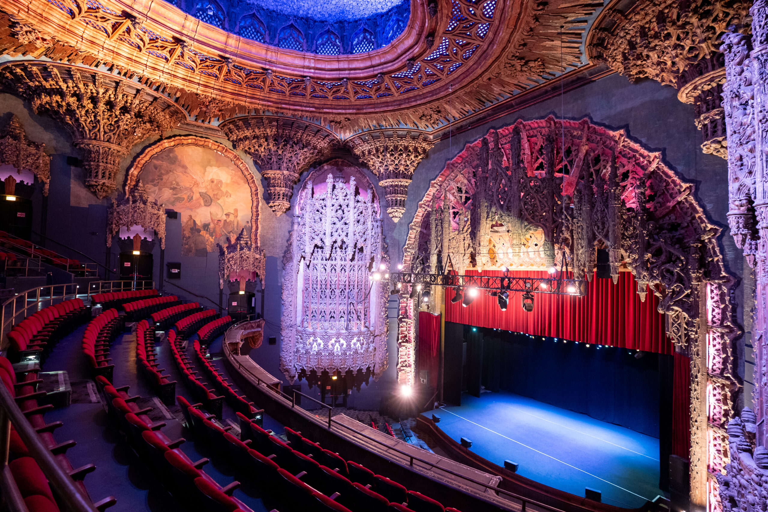 View from a mid-orchestra seat toward a proscenium stage in a Broadway-style theater, with rows of seats and warm house lights